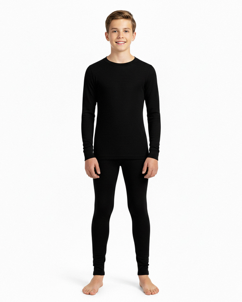 A boy wearing a black long-sleeve Merino wool base layer top and matching leggings, standing barefoot in a white studio.