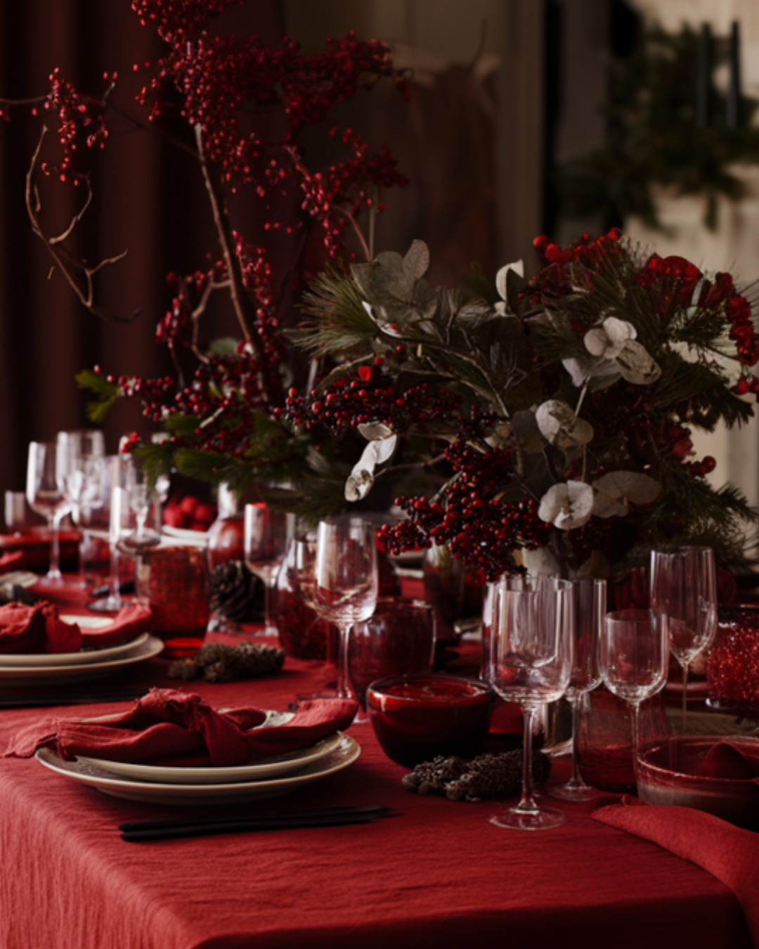 Decorative table setting with red tablecloth, glasses, and floral arrangements.