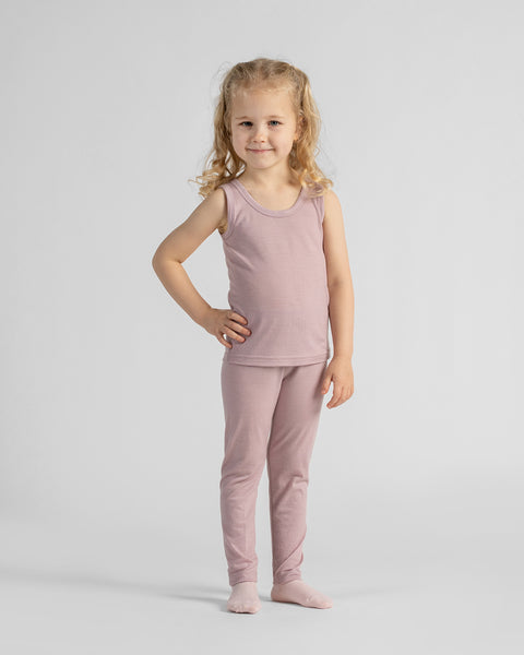 Full-length portrait of a young blonde girl standing barefoot with one hand on her hip, wearing a dusty rose sleeveless tank top and matching leggings.