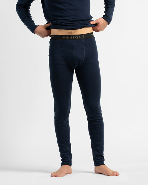 A full-body view from the chest down of a barefoot man standing against a white studio background, wearing a navy long-sleeve thermal base layer set.