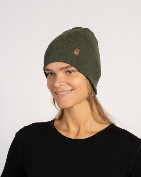Woman smiling in a dark green knitted Merino wool beanie, angled view.