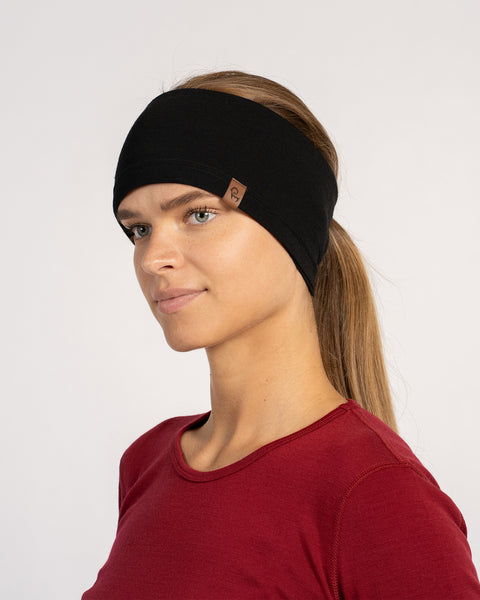 Woman wearing a black Merino wool headband, paired with a red top, looking to the side.