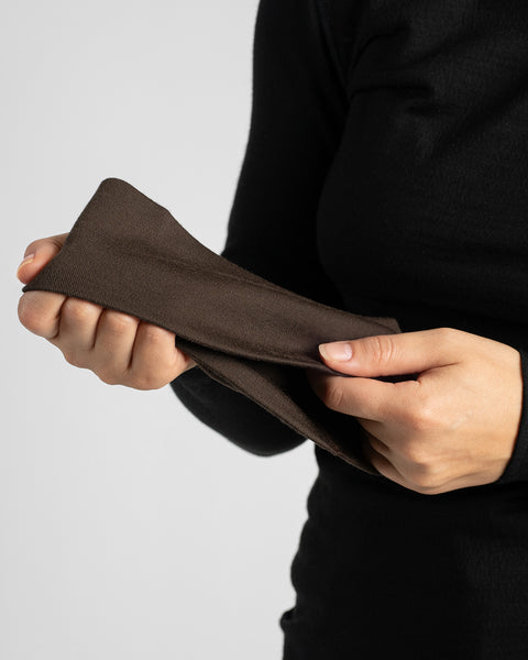 A close-up view of hands demonstrating the texture and stretch of a dark brown knit fabric headband.