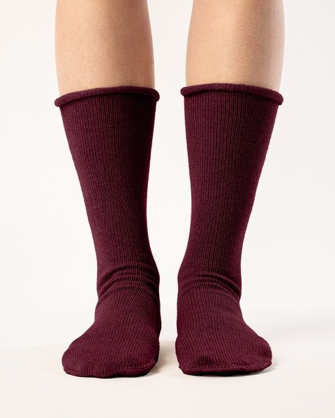 A person is shown from the mid-thigh down, wearing ribbed, royal cherry colos socks. The socks are pulled up to the mid-calf, and the person's feet are slightly apart against a plain white background. The lighting is even, highlighting the texture of the socks.