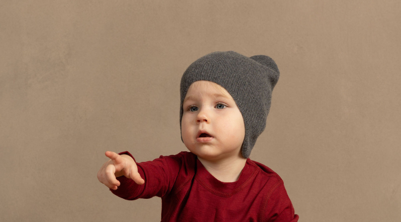 A baby girl wearing a royal cherry long sleeve merino wool shirt and a perfect gray merino wool knit beanie, pointing her finger at something.