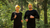 a couple running in the forest, wearing matching merino clothing and accessories. They are wearing black merino long sleeve tops. The attention is caught by the power mango (bright yellow) shade headbands.