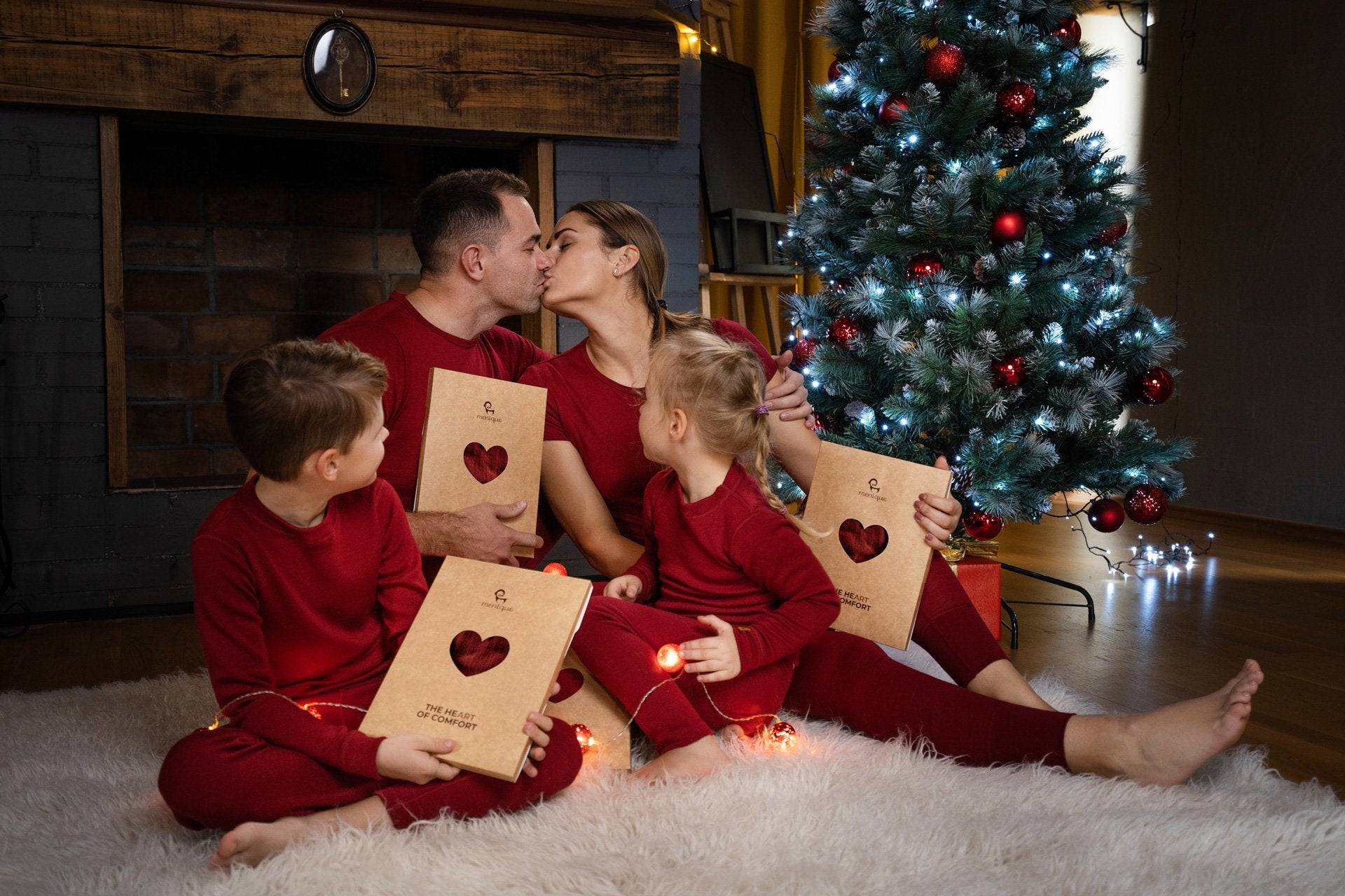 Happy family sitting near a Christmas tree in matching red color clothes and exchanging gifts.  