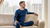 A man wearing the menique merino wool mid layer denim clothing set of 250gsm fabric. It includes a long sleeve shirt and pants. He is sitting down on a couch.