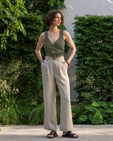 A woman wearing 100% linen sleeveless wrap crop top in the color stone green and high-waisted pants lotus in the color natural. 