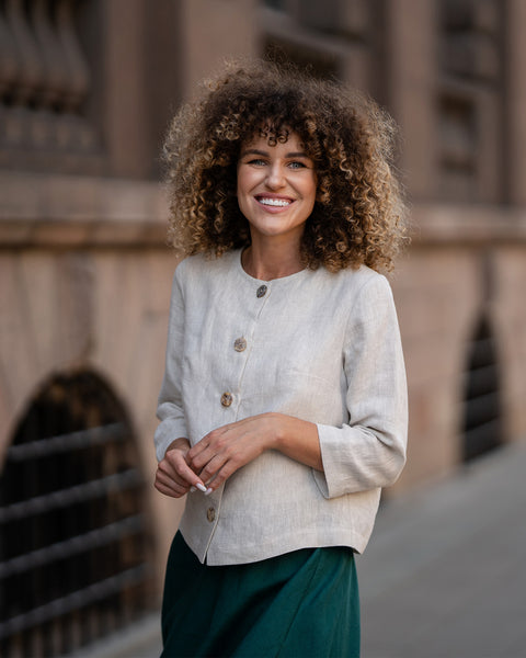 A model wearing a natural beige linen jacket Alice with buttons, featuring a relaxed fit, 3/4-length sleeves, and a minimalist design. The jacket is paired with matching dark green skirt