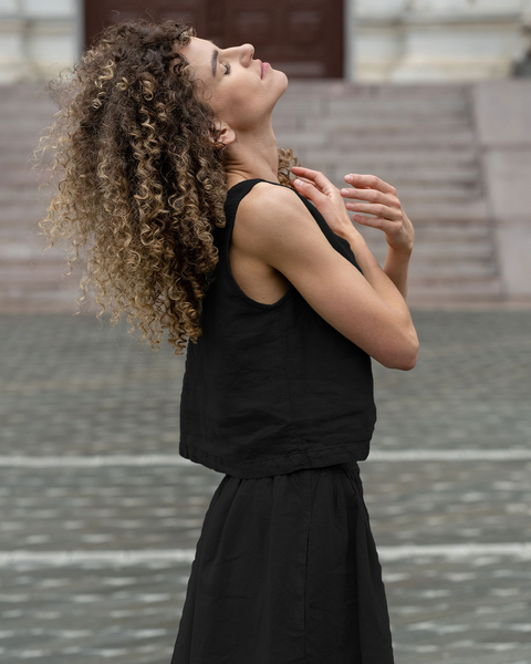 Woman wearing black linen sleeveless top and matching linen skirt, lightweight breathable summer co-ord set with minimalist silhouette styled outdoors