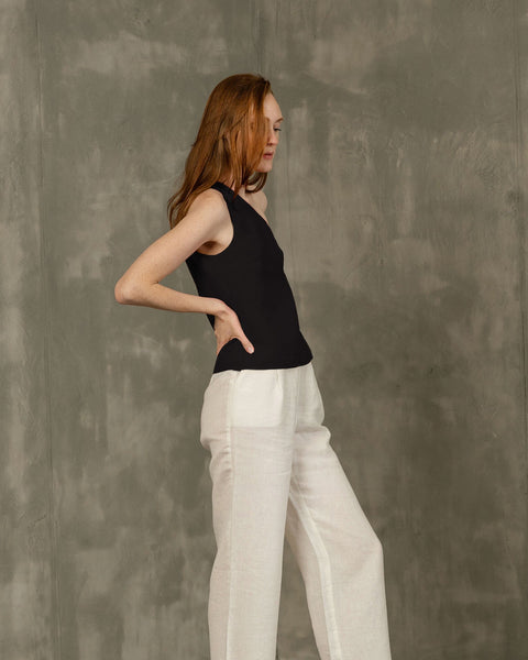 A woman with long reddish hair in a pure black menique sleeveless top and linen pants.