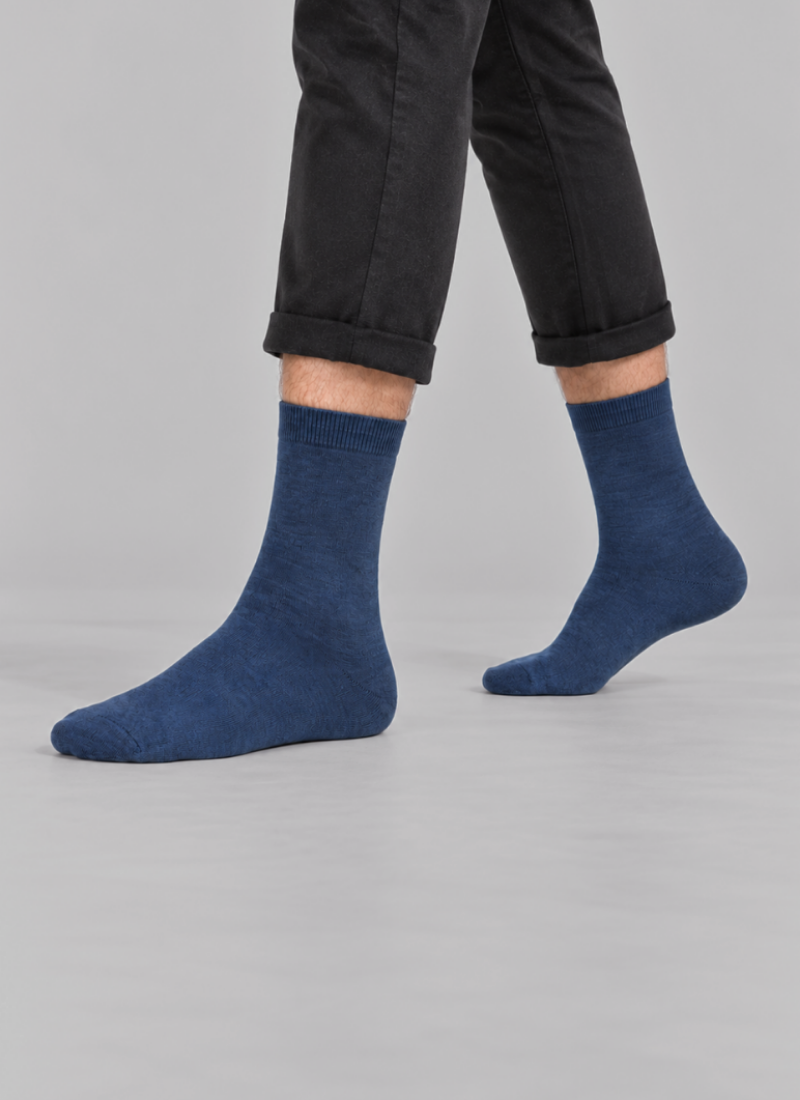 A person is shown from the knees down, wearing cropped black pants and dark navy blue crew socks. They are standing against a plain light grey studio background.