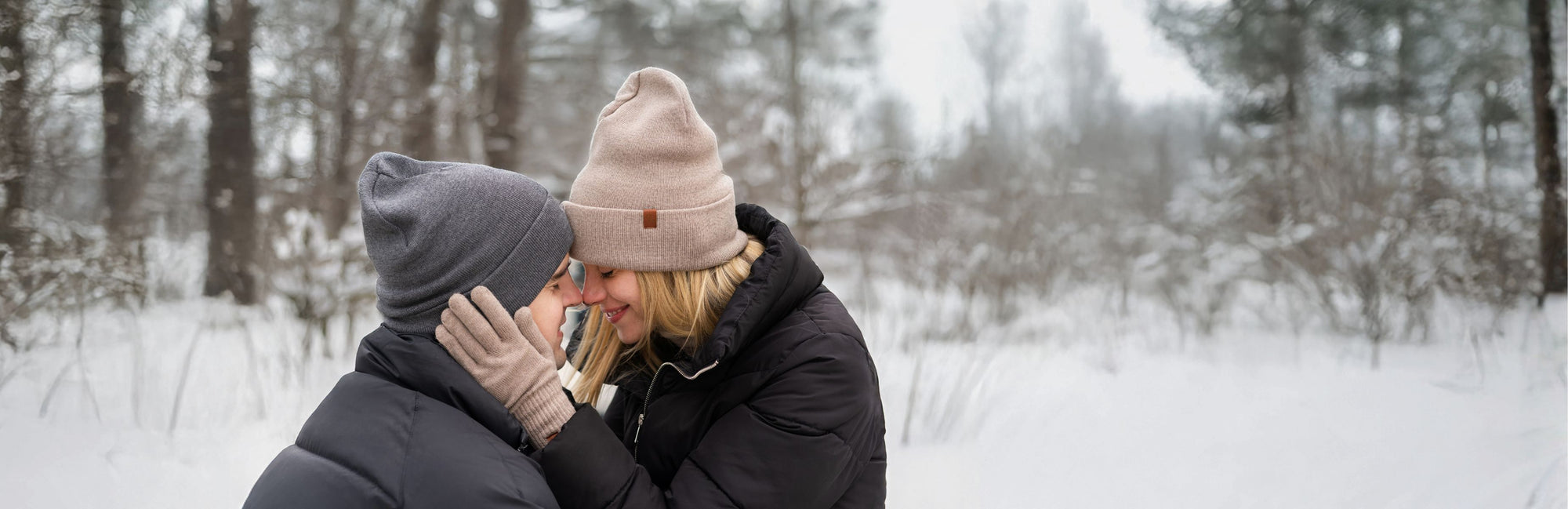 Two people in winter clothing embracing in a snowy forest.