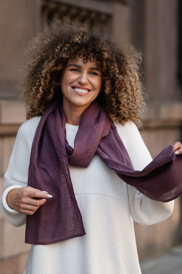 Elegant plum-colored European washed linen scarf draped over white knit sweater showing lightweight fabric texture by Menique