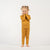 A young child with curly blonde pigtails, wearing a yellow long-sleeved top and matching pants, stands barefoot on a white background, looking directly at the camera with a gentle smile.