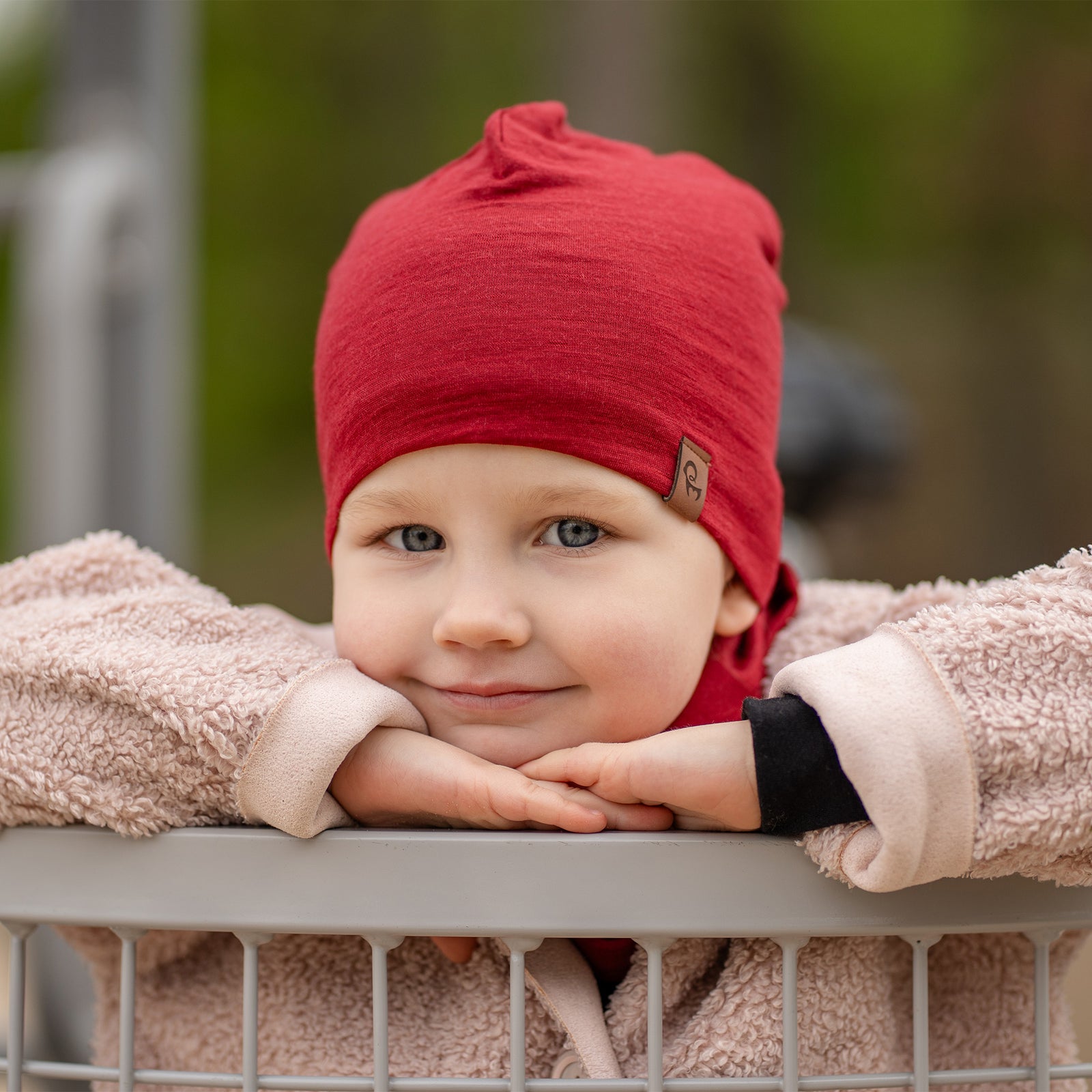 Smiling child playing outdoors wearing a black Merino wool kids’ beanie and matching neck gaiter, cozy beige coat, playground background.