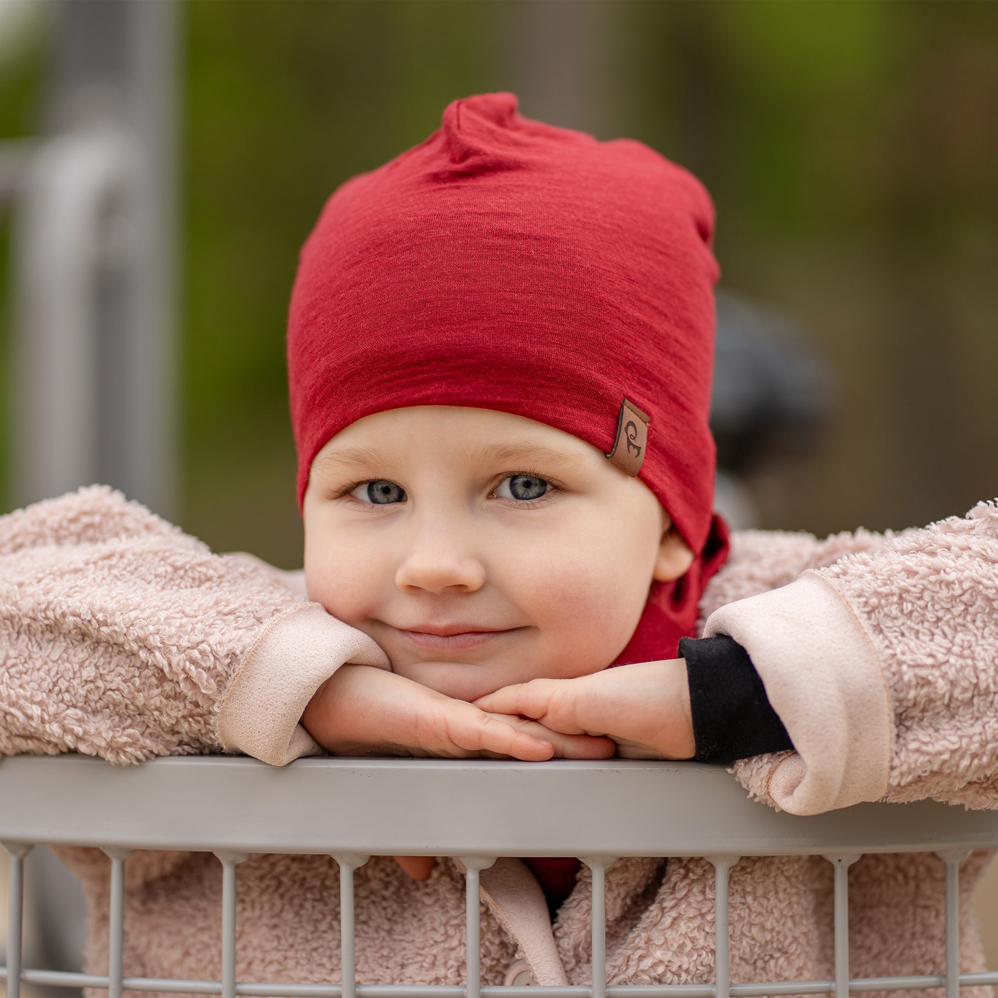 Smiling child playing outdoors wearing a black Merino wool kids’ beanie and matching neck gaiter, cozy beige coat, playground background.