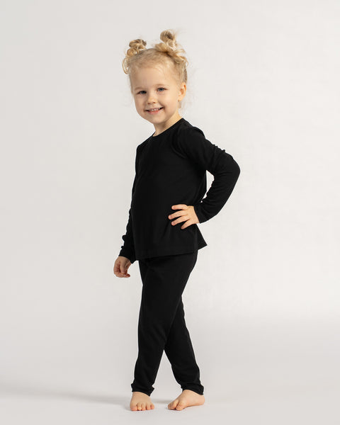 Child standing in black bamboo long sleeve shirt and leggings, showing flexible fit and everyday comfort.