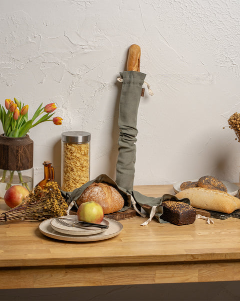 Wooden table with bread, apples, and kitchen items against a light wall.