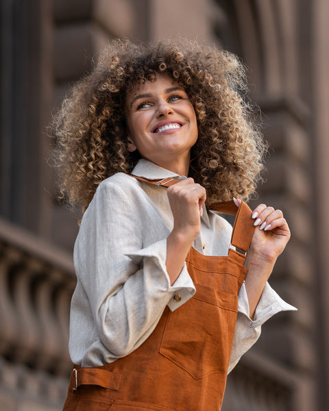 Woman with curly hair standing in a street and wearing Linen Pinafore Jumpsuit Nicci Almond Brown