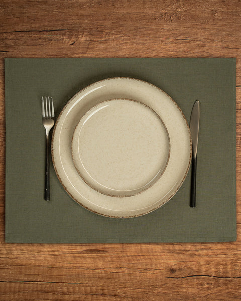The menique linen placemat in stone green color on a wooden table top. 