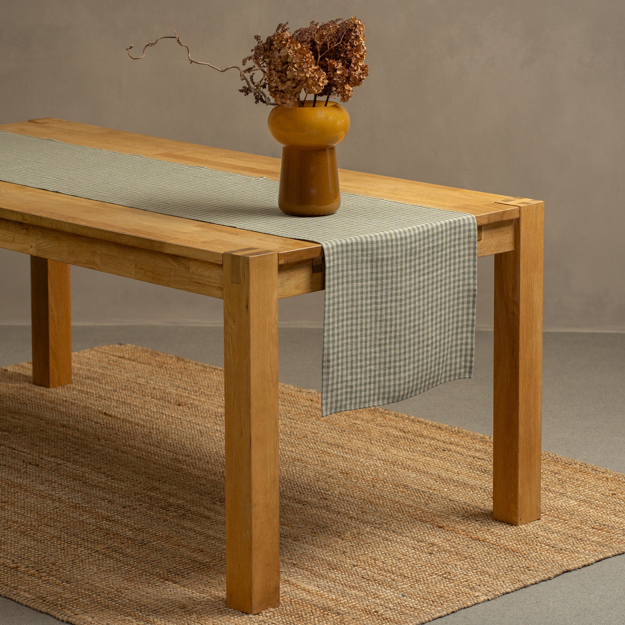 The menique natural linen table runner on top of a green check tablecloth. 