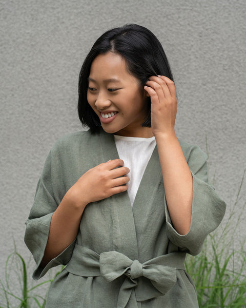 Woman with short dark hair wearing a stone green linen jacket and stone green menique pants.