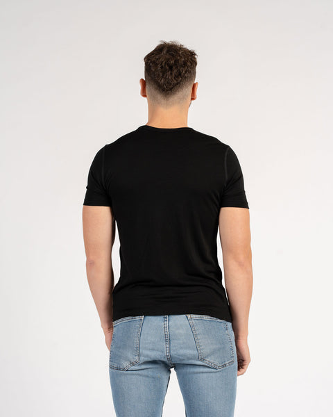 Back view of man wearing a black slim fit Merino wool t-shirt with blue jeans.