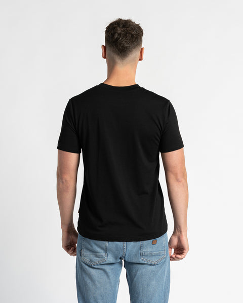 Back view of a man wearing a black t-shirt and light blue jeans, standing against a white background. The black t-shirt is the primary focus, showcasing its regular fit and design from the rear. The man is positioned centrally, displaying the back of the garment clearly.
