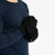 A person wearing a dark blue long-sleeved shirt and black menique mittens with a flap that can cover the fingers, turning them into mittens. The person is holding their hands together, and the flap on one glove is pulled back, exposing the fingers, while the flap on the other glove covers the fingers.