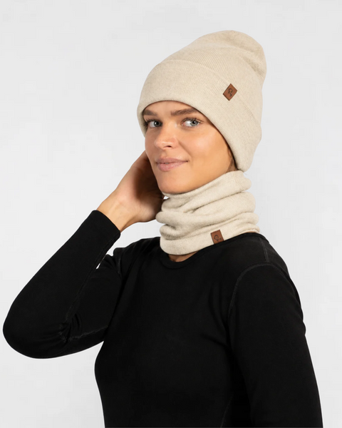 Woman wearing a natural knit beanie, matching gloves, and a neck gaiter covering her face, dressed in a black long-sleeve top.