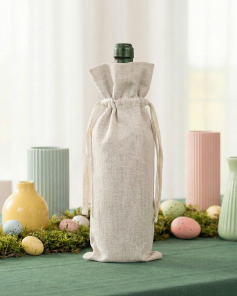 Wine bottle wrapped in a natural linen drawstring gift bag displayed on a spring table with pastel eggs and ceramic vases.