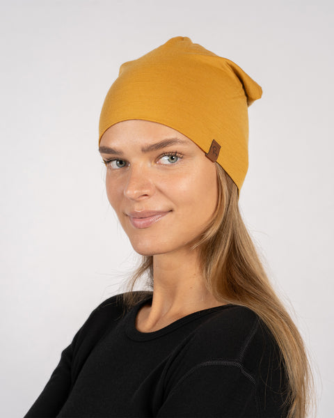 Side view of woman in yellow merino beanie, smiling slightly.