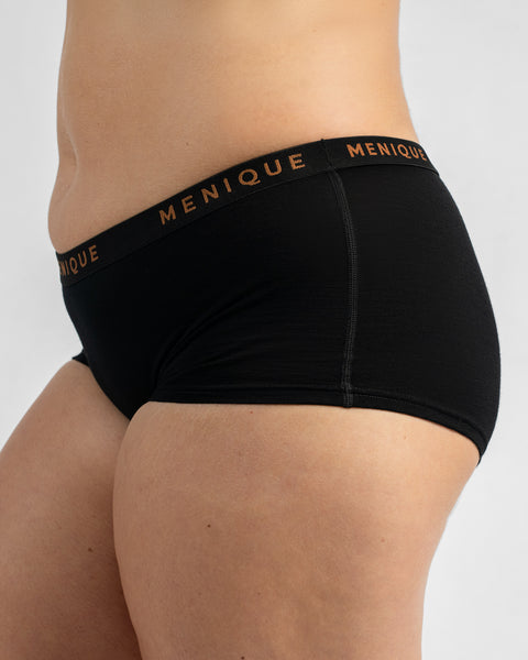 Side profile view of a model wearing black boy-short underwear with a black elastic waistband featuring text.