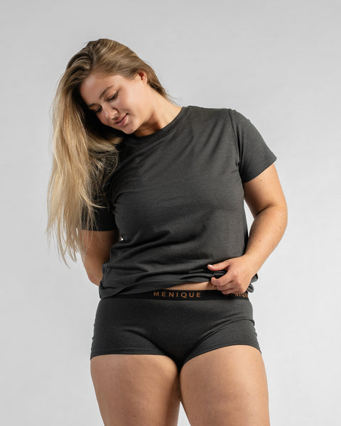 Front three-quarter view of a model with long blonde hair wearing a dark grey short-sleeve t-shirt and dark grey boy-short underwear, looking downwards.