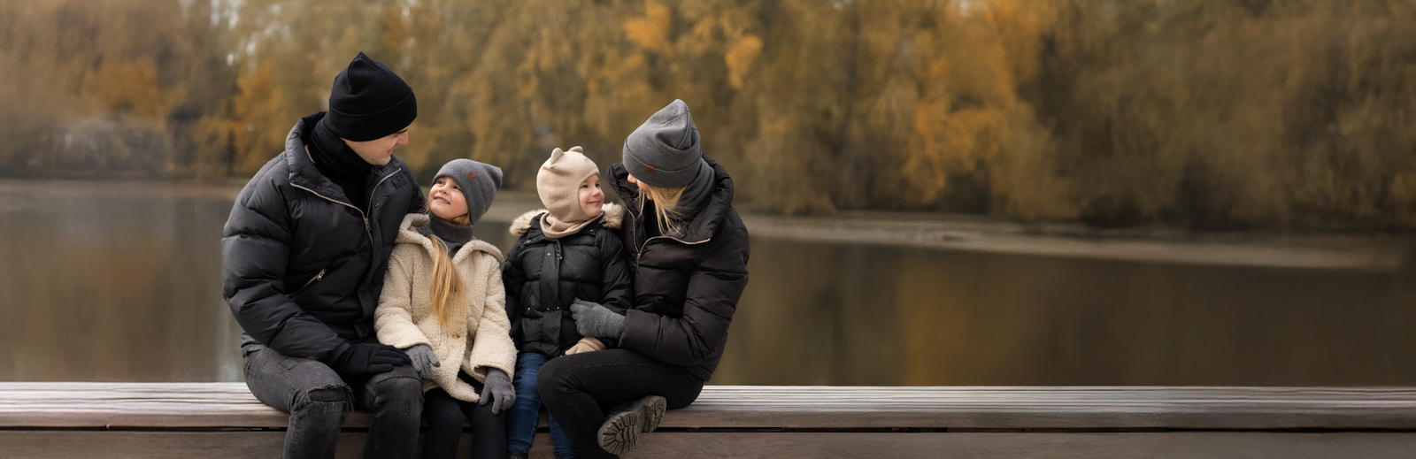 Family of four sitting on a bench by a lake with autumn foliage.