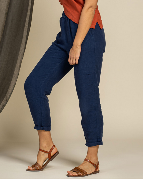 Person wearing storm blue linen menique pants and brown sandals on a neutral background