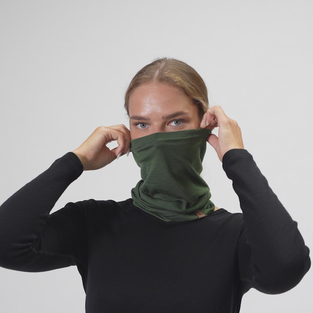 Woman puts Merino wool neck gaiter in dark green color on her face