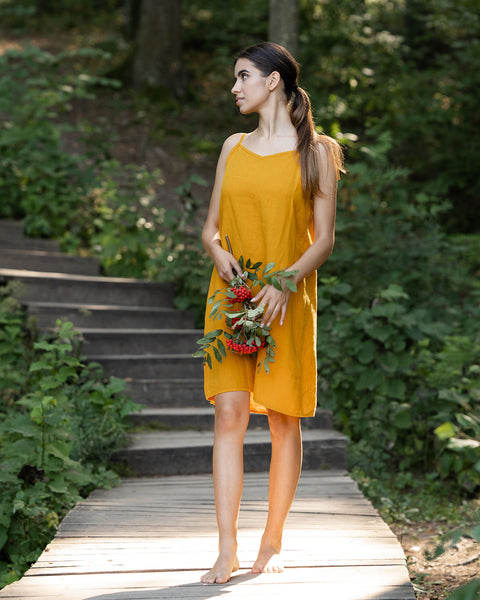 Woman wearing spicy yellow linen dress and standing in  the forest