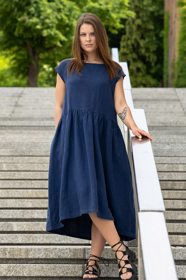 Young woman posing in a city street on stears wearing linen smock dress cecilia in a storm blue color. Girl with a cat tattoo on her left arm.