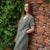 Young woman posing near the red brick wall, wearing stone green color linen tunic dress Joelle.