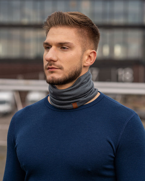 a man wearing the menique unisex neck gaiter in perfect gray color. He is outside, dressed in a long sleeve merino top in dark blue color.